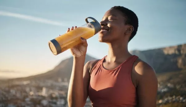 Mulher bebendo de uma garrafa esportiva ao ar livre, com a cidade ao fundo