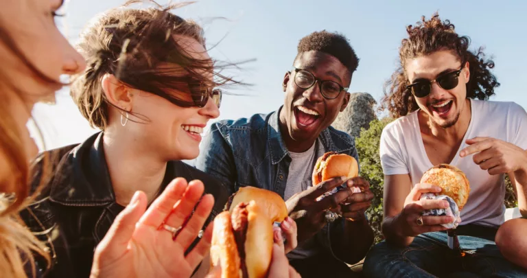 Grupo de jovens rindo e comendo hambúrgueres ao ar livre