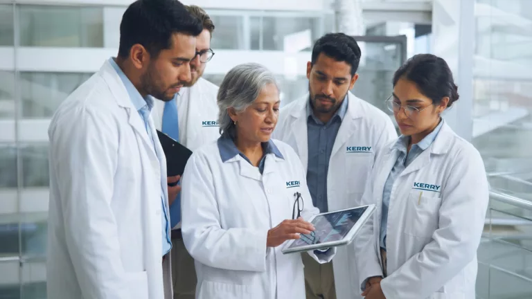 Equipe técnica de jaleco discutindo dados em um tablet dentro de uma planta industrial