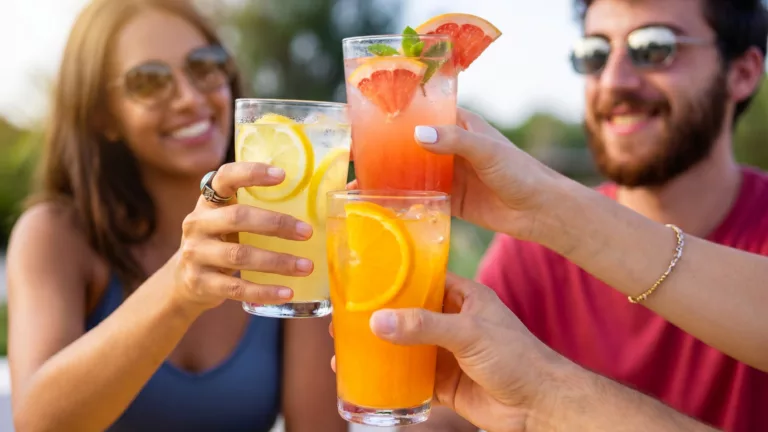 Amigos brindando com bebidas cítricas de limão e laranja em copos com gelo